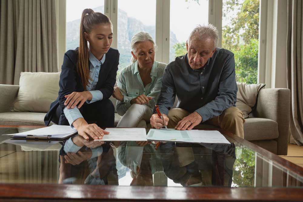 Older couple reviewing and signing estate planning documents with a legal advisor at home, illustrating estate planning for blended families in Oklahoma.